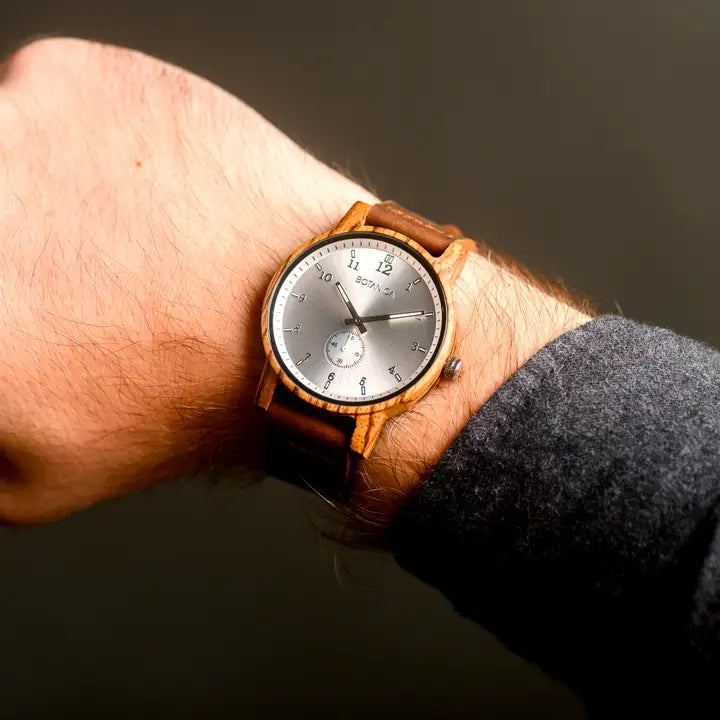 Wooden wristwatch with a silver face on a wrist against a dark background