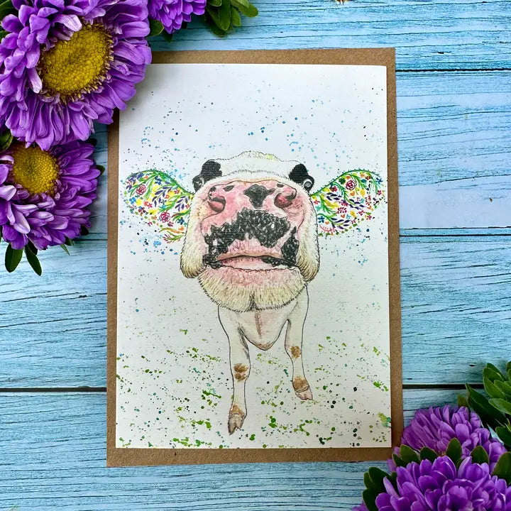 Card with a colorful illustration of a cow on a blue wooden background with purple flowers.
