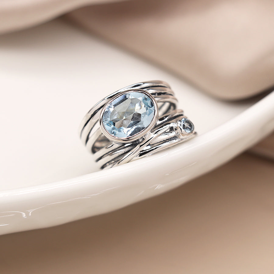 Silver ring with a blue gemstone on a white ceramic dish