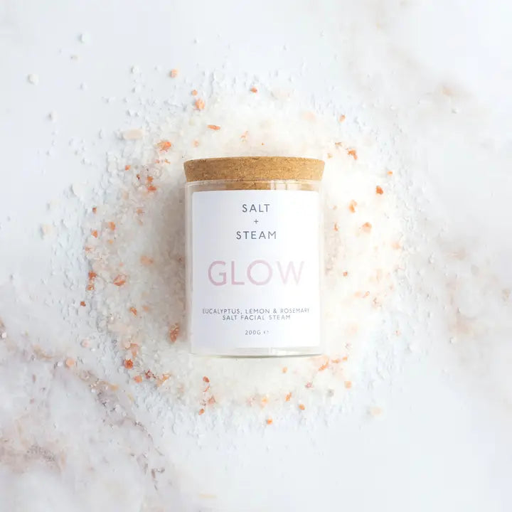Candle labeled 'Salt + Steam Glow' on a white surface with pink salt crystals.