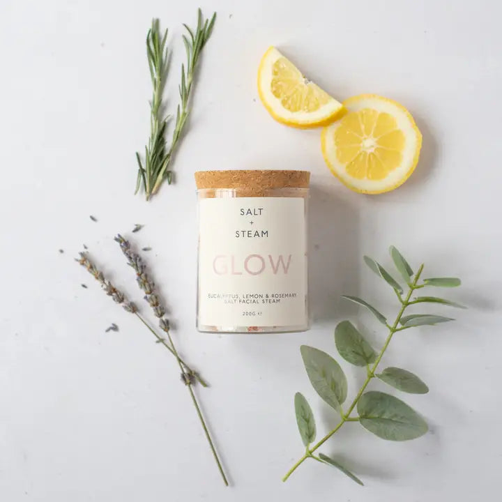Candle labeled 'Salt & Steam Glow' with lemon slices and herbs on a light background