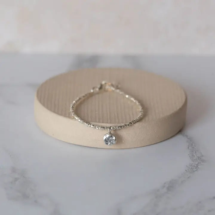 Silver bracelet with a heart charm on a beige stand against a marble background