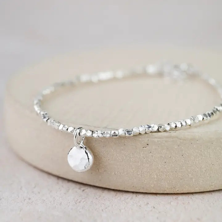 Silver bracelet with a small round charm on a light beige background