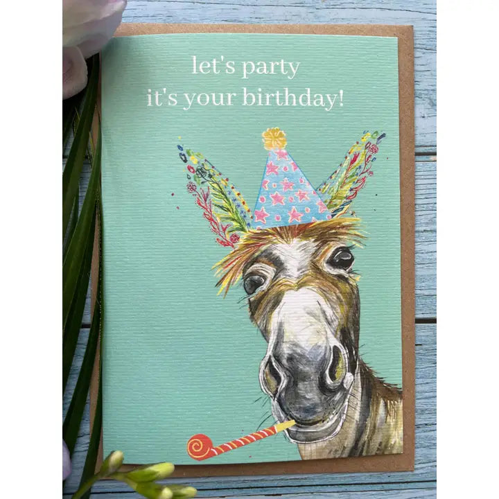 Birthday card with a donkey wearing a party hat and the text 'let's party it's your birthday!' on a wooden surface.