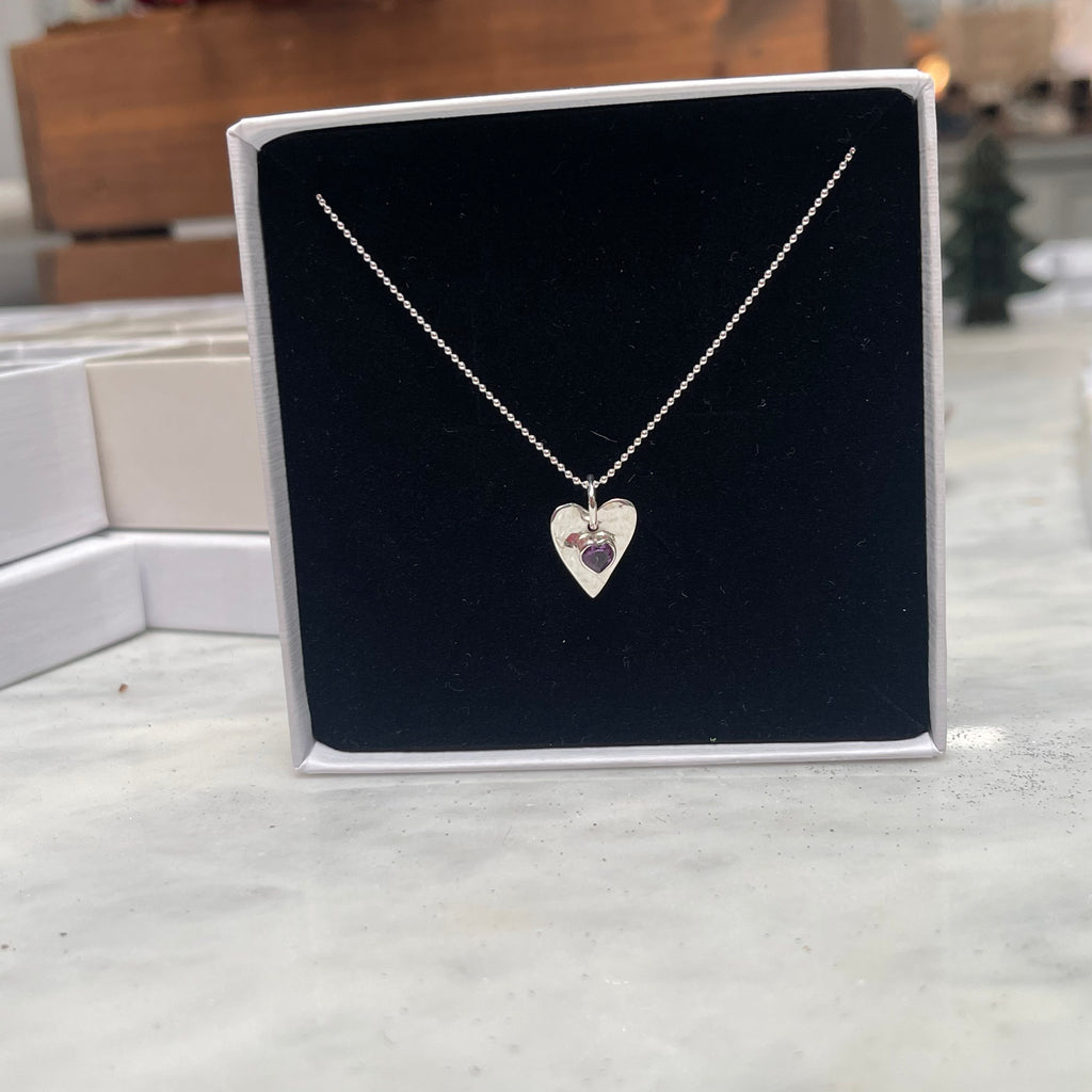 Silver necklace with a heart pendant on a black card, displayed on a marble surface.