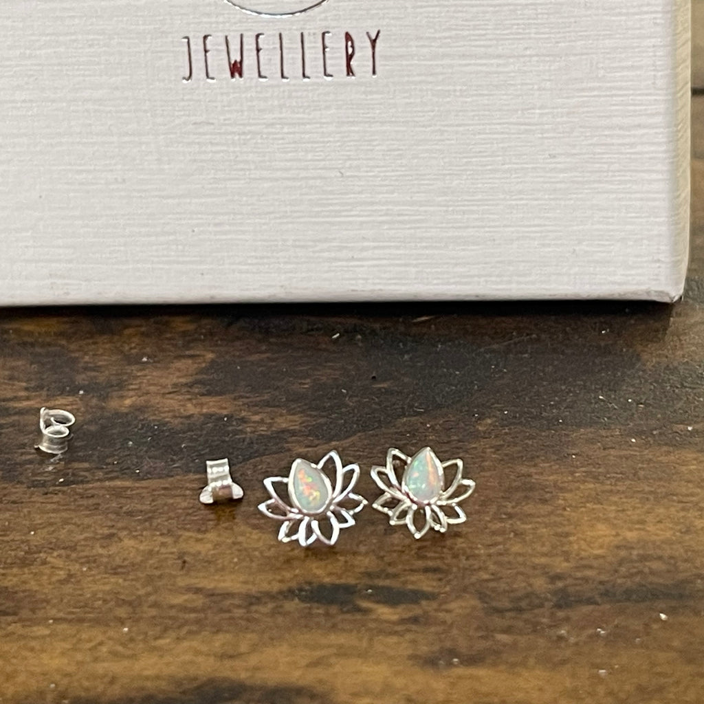Silver lotus flower earrings on a wooden surface with 'Jewellery' box in the background.
