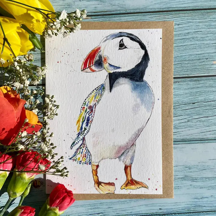 Card with a puffin illustration on a wooden surface with flowers.