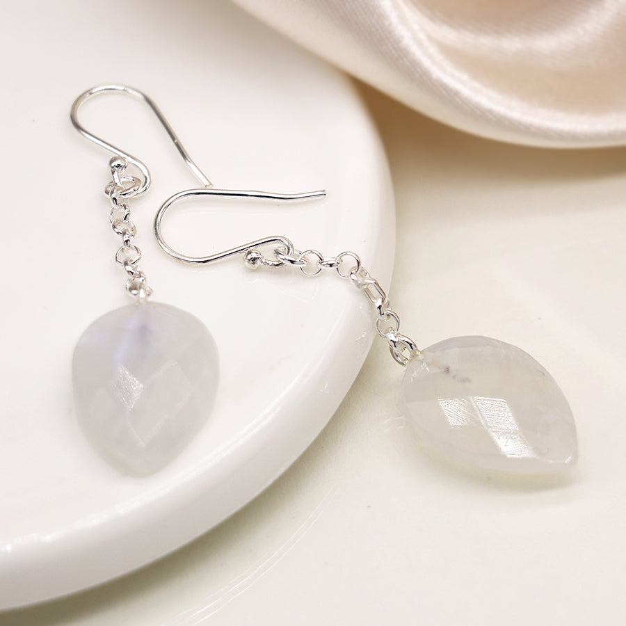 Silver earrings with heart-shaped gemstones on a white dish