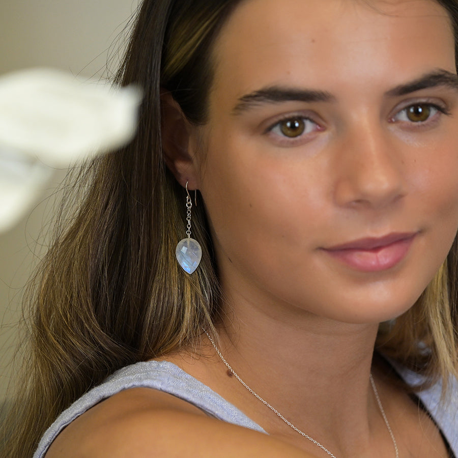 Close-up of a woman wearing a silver earring with a teardrop-shaped gemstone.