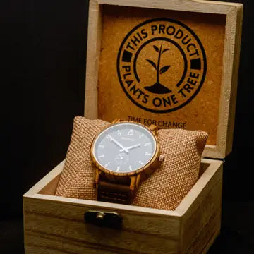 Wooden watch with a textured strap in a wooden box, featuring a logo that reads 'This Product Plants One Tree'.