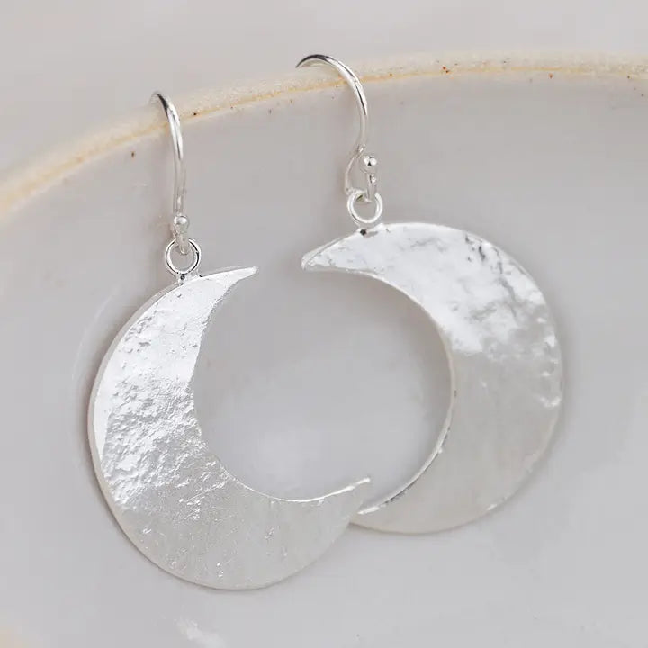 Silver crescent moon earrings on a white ceramic plate