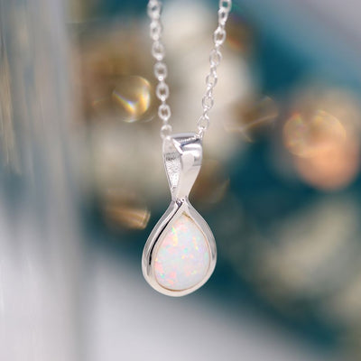 A white opal teardrop pendant necklace with a silver chain, displayed against a blurred background.